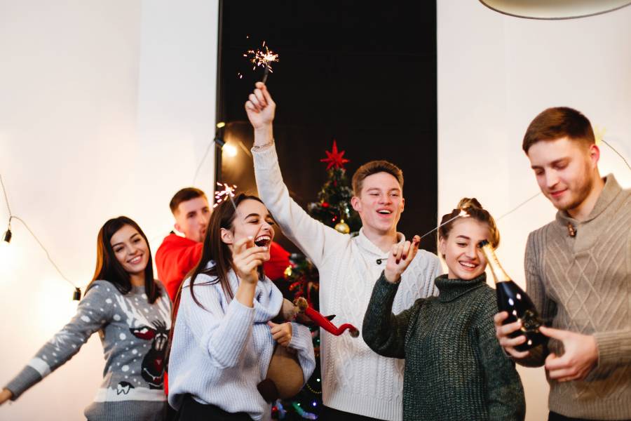 Christmas and New Year preparetions. Company of attractive happy young people celebrate clanging glasses and dancing around the Christmas tree